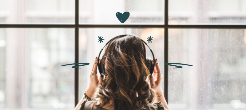 Back of a woman's head with long brown hair, with headphones on and her hands over the earpads